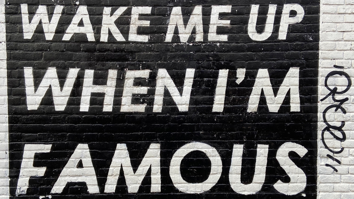 "Wake me up when I'm famous" quoted in light text on a dark brick wall.