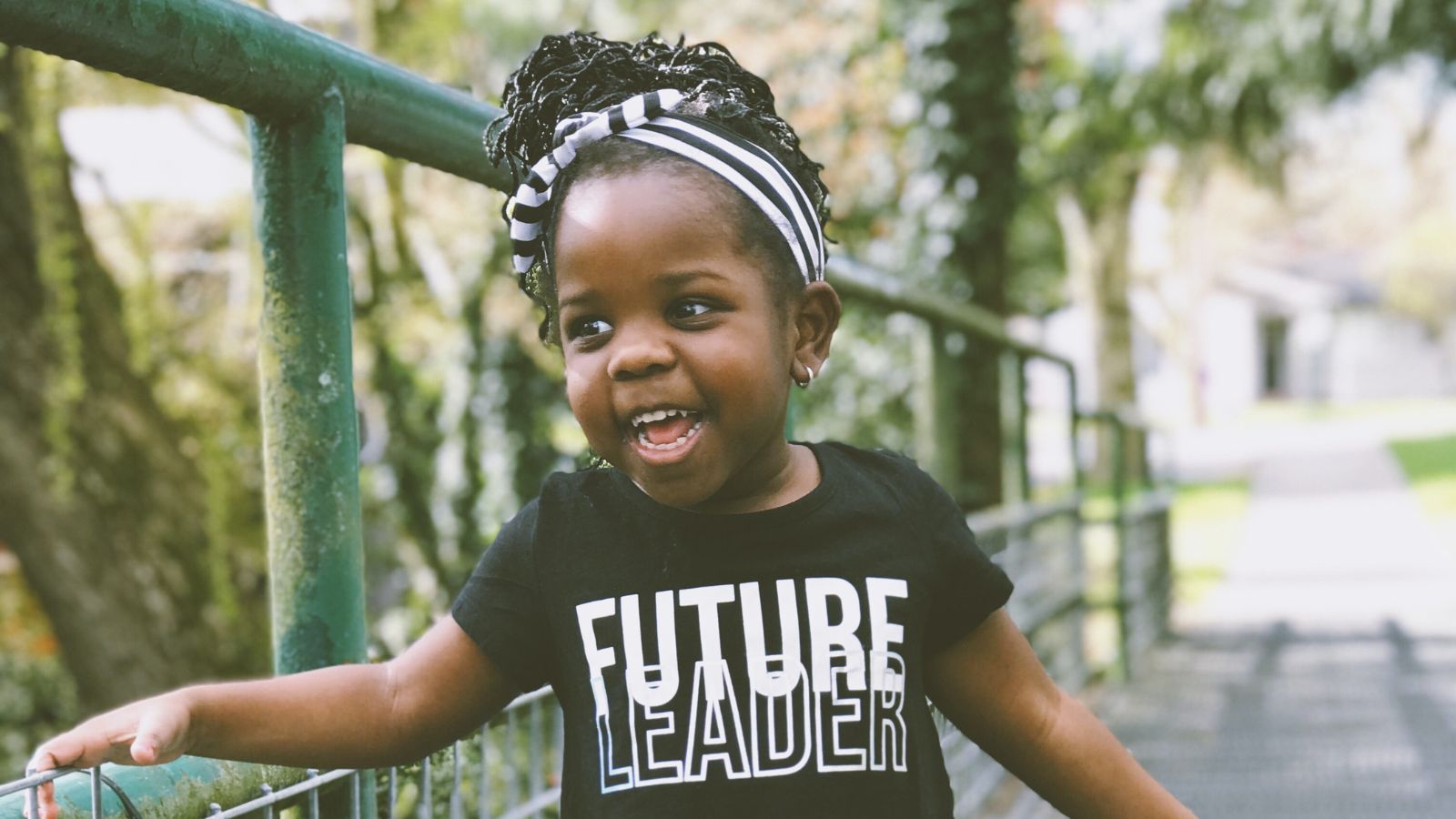 black toddler aged girl playing outside wears a dark t-shirt that reads "future leader" in light writing.