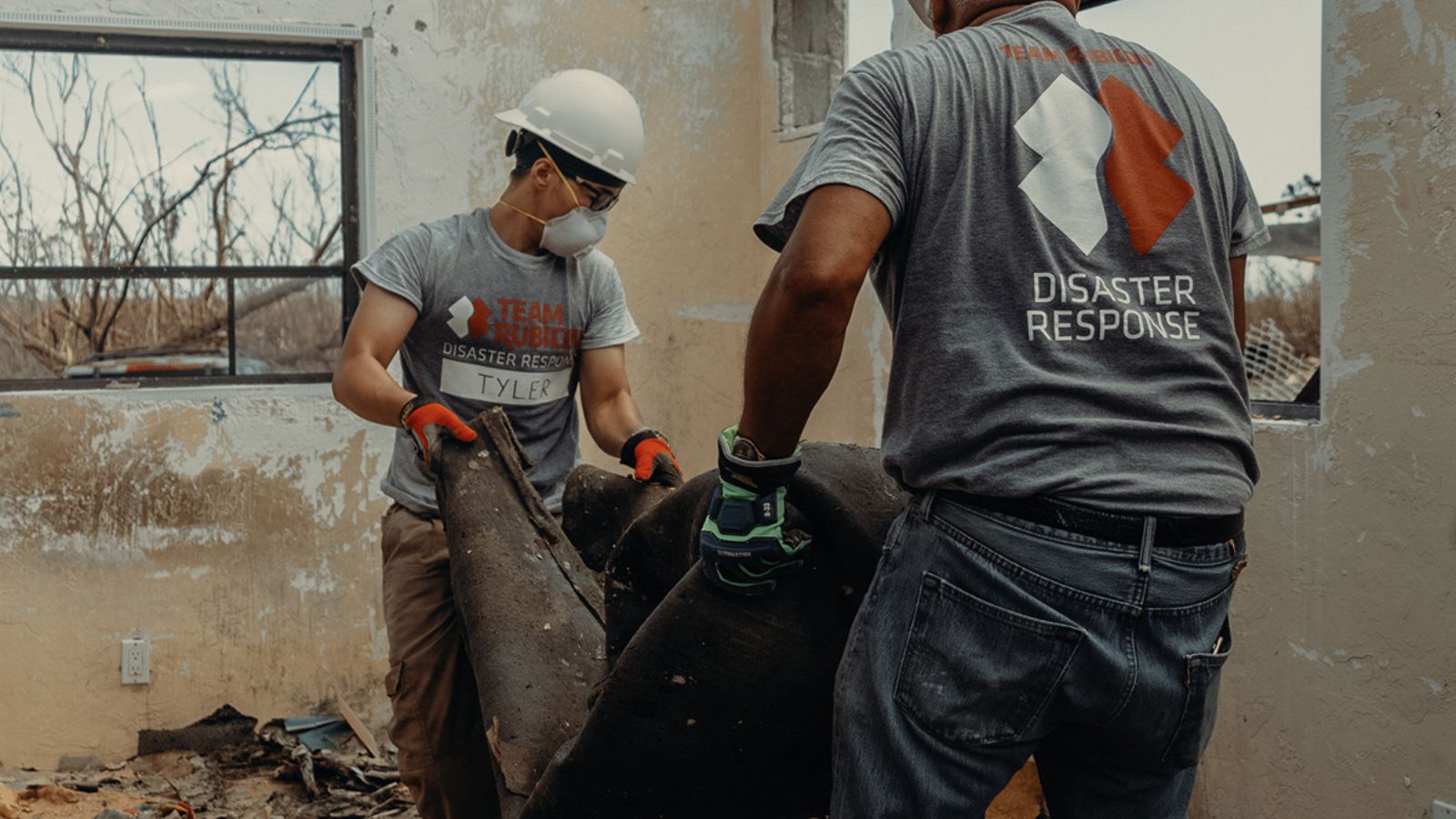 Two volunteers in a home hit by a natural disaster, carrying away rubble.