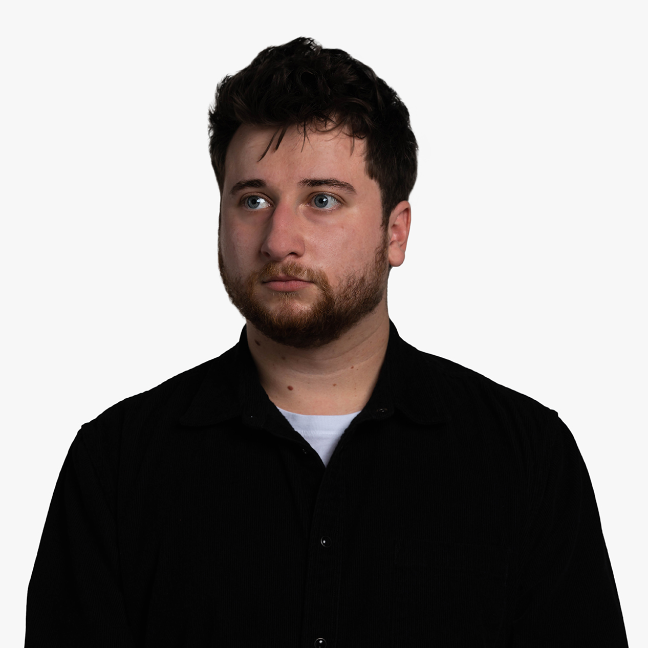 Bret Caples, a white man with messy brown hair wearing a black corduroy shirt. The photo is not the best representation of him and he looks uncomfortable.