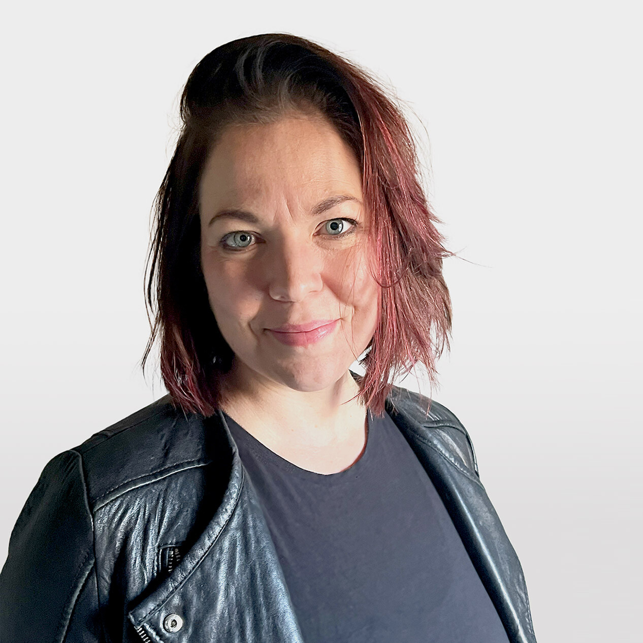 Nina Earley, a white woman in her late thirties with reddish brown chin-length hair and blue eyes, wearing a black shirt and leather jacket, smiling slightly and looking at the camera.
